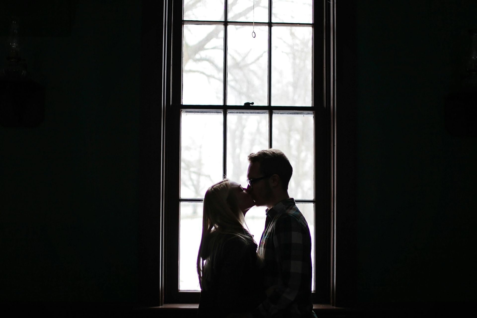 Couple kissing silhouetted in front of a window.