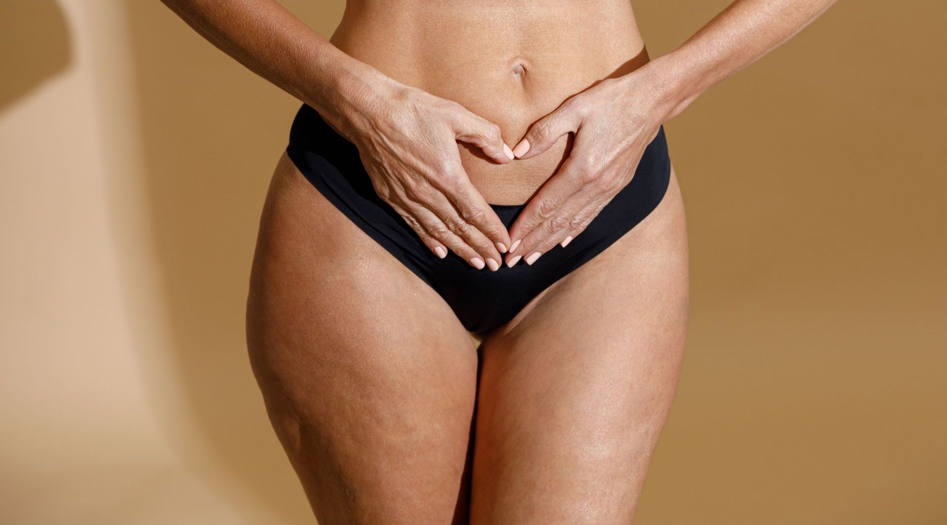 A woman is making a heart shape with her hands on her stomach.