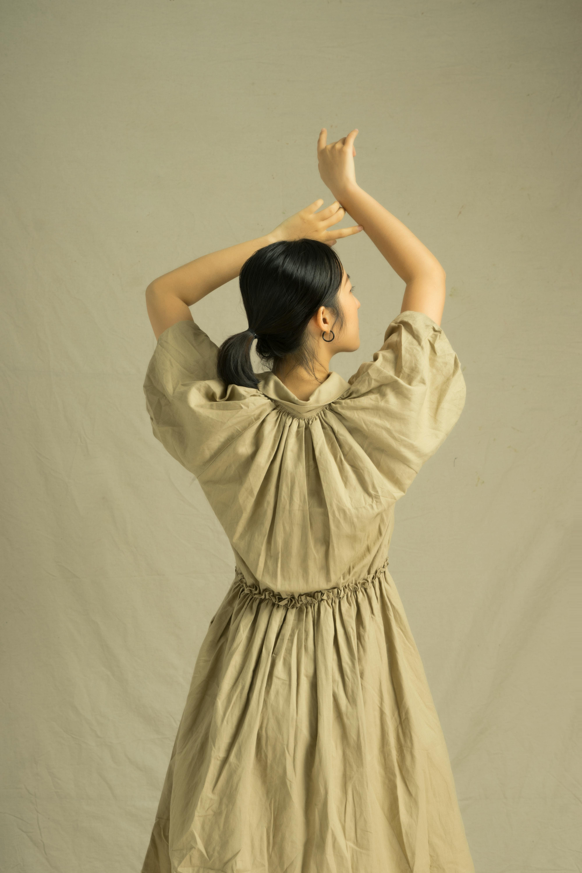 A woman in a beige dress stretching her arms gracefully, symbolizing relaxation, growth, and business success.
