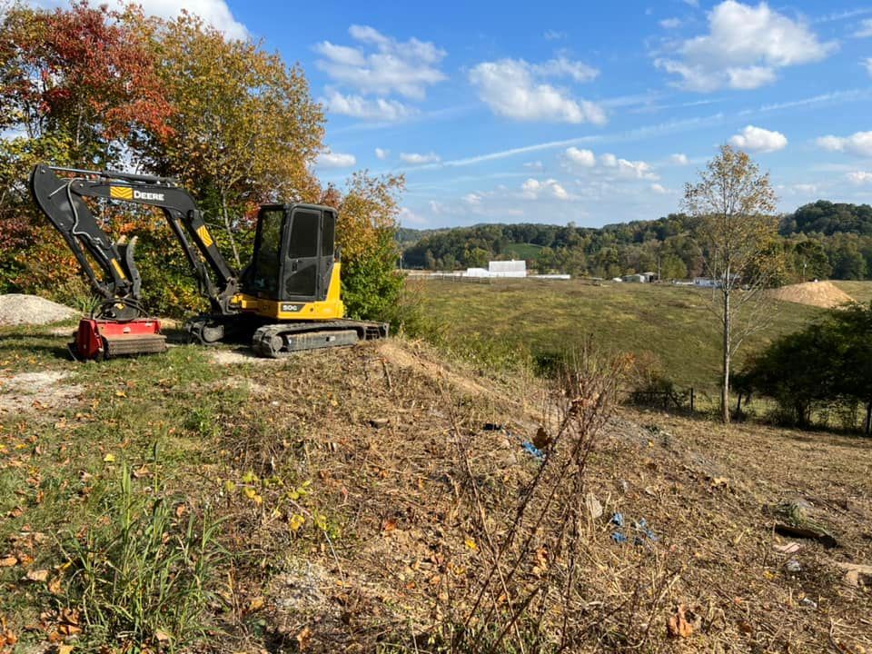 A small excavator is sitting on top of a hill in a field.