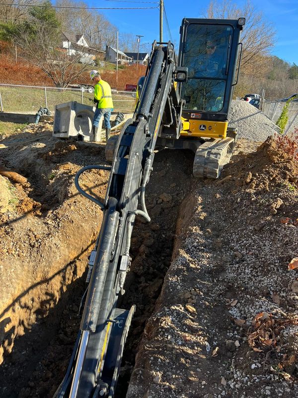 A yellow excavator is digging a trench in the dirt.