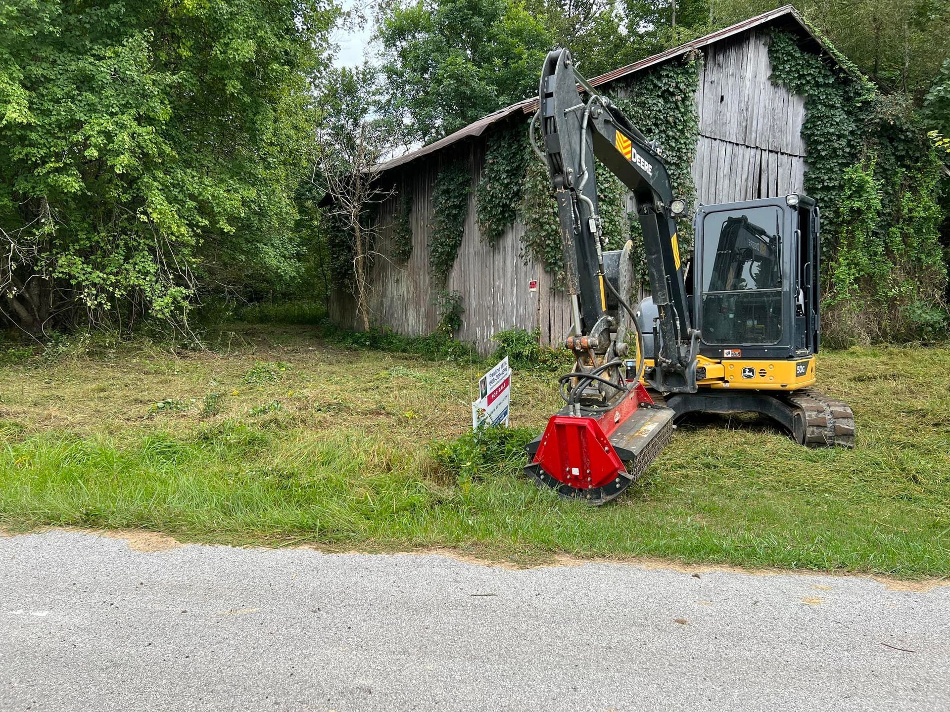 A small excavator is cutting grass in front of a house.