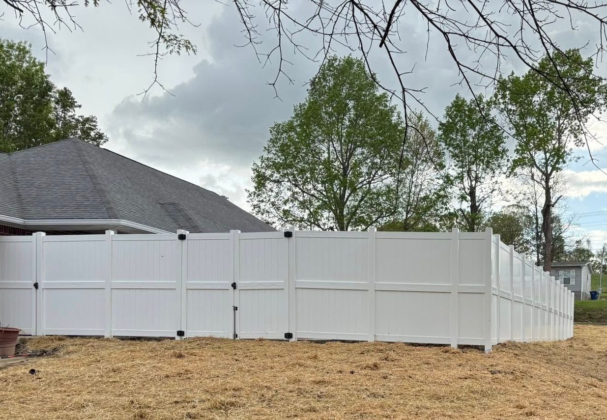 A white fence surrounds a dirt field in front of a house.