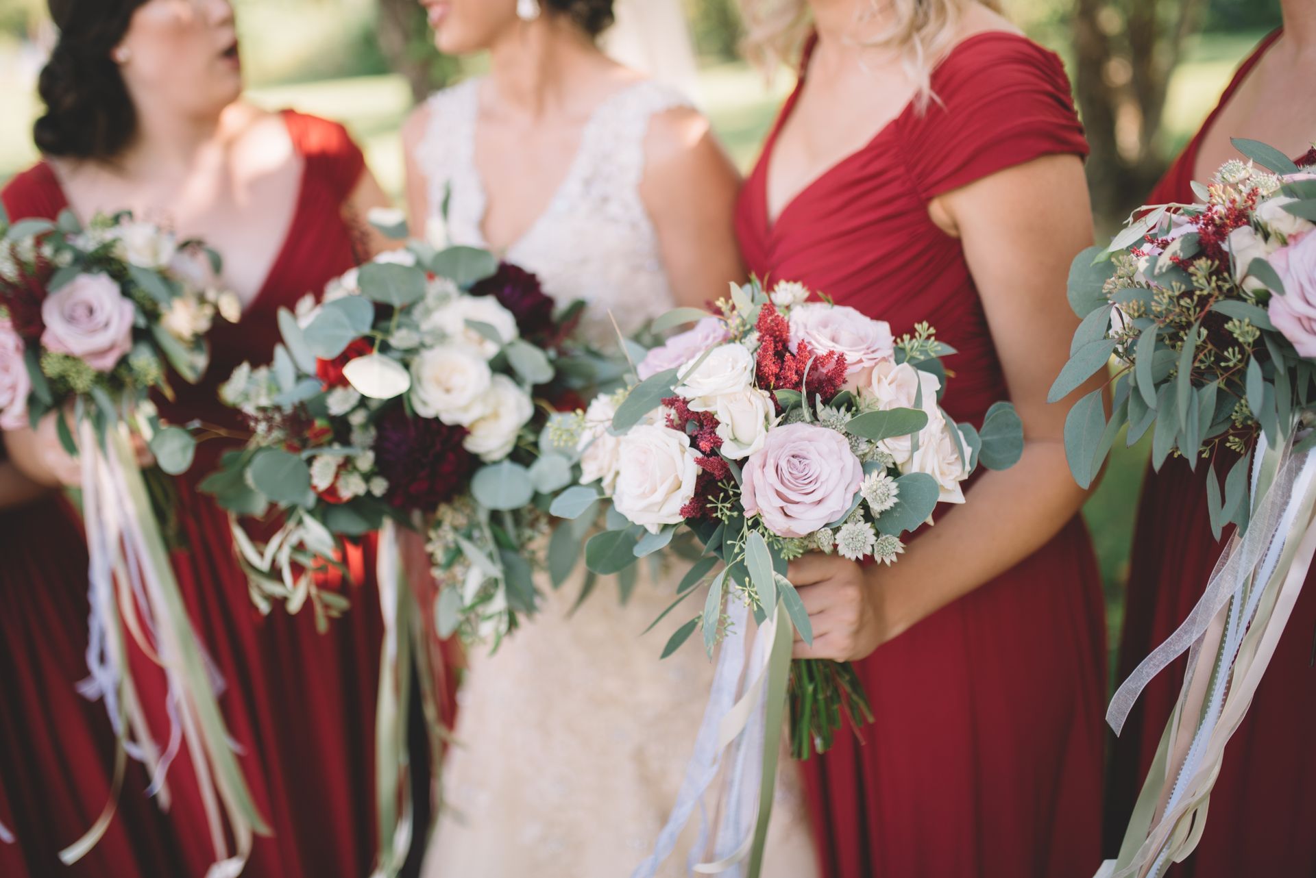 Bridesmaids in red dresses holding bouquets with roses and greenery.