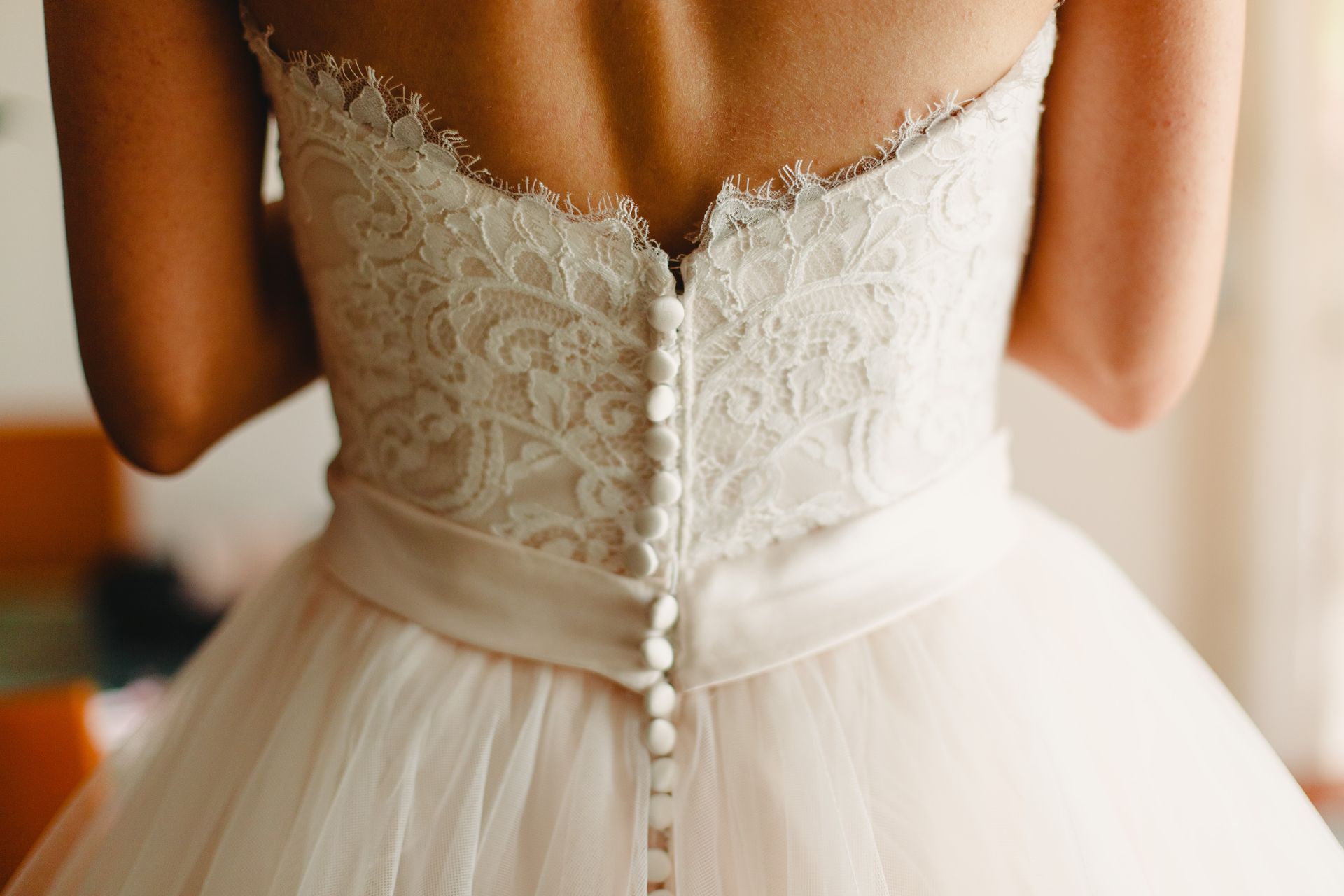 Woman wearing a white wedding dress, back view, with lace bodice and button details.