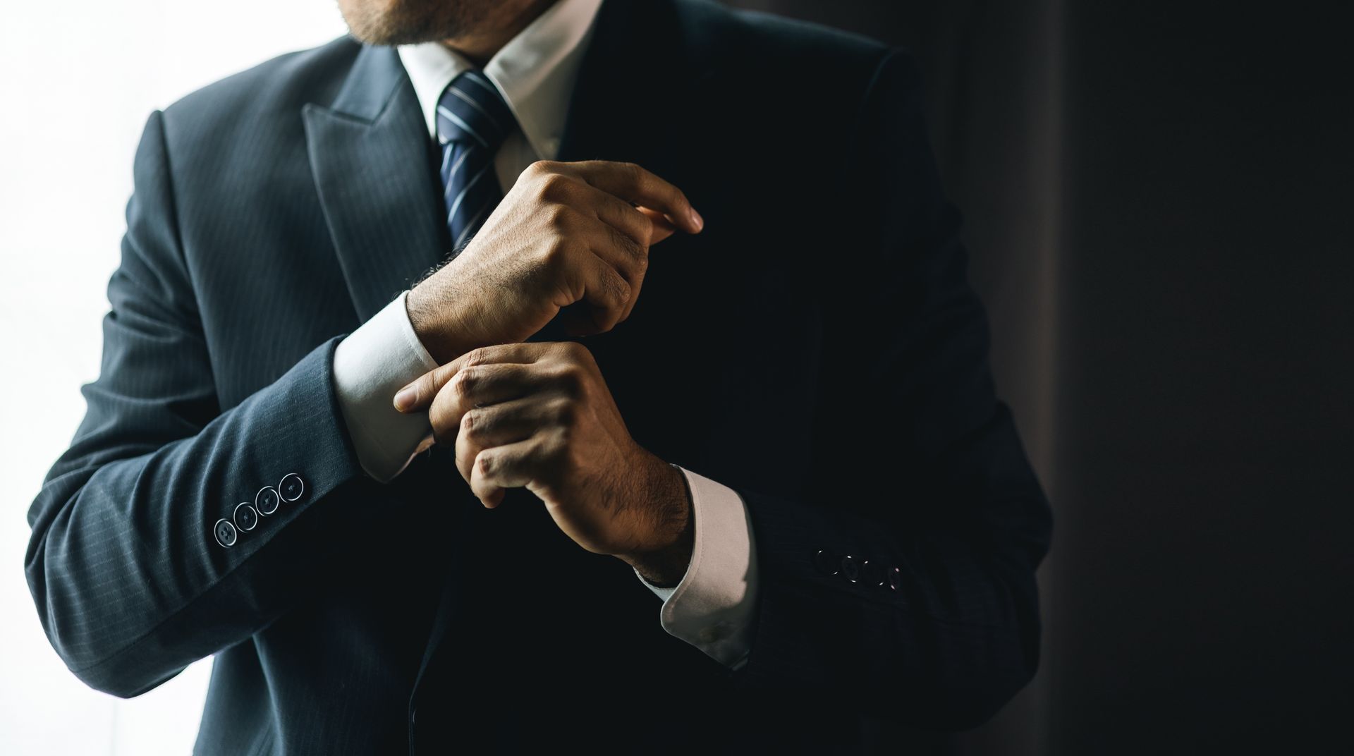 Man in a dark suit adjusting his cufflink.