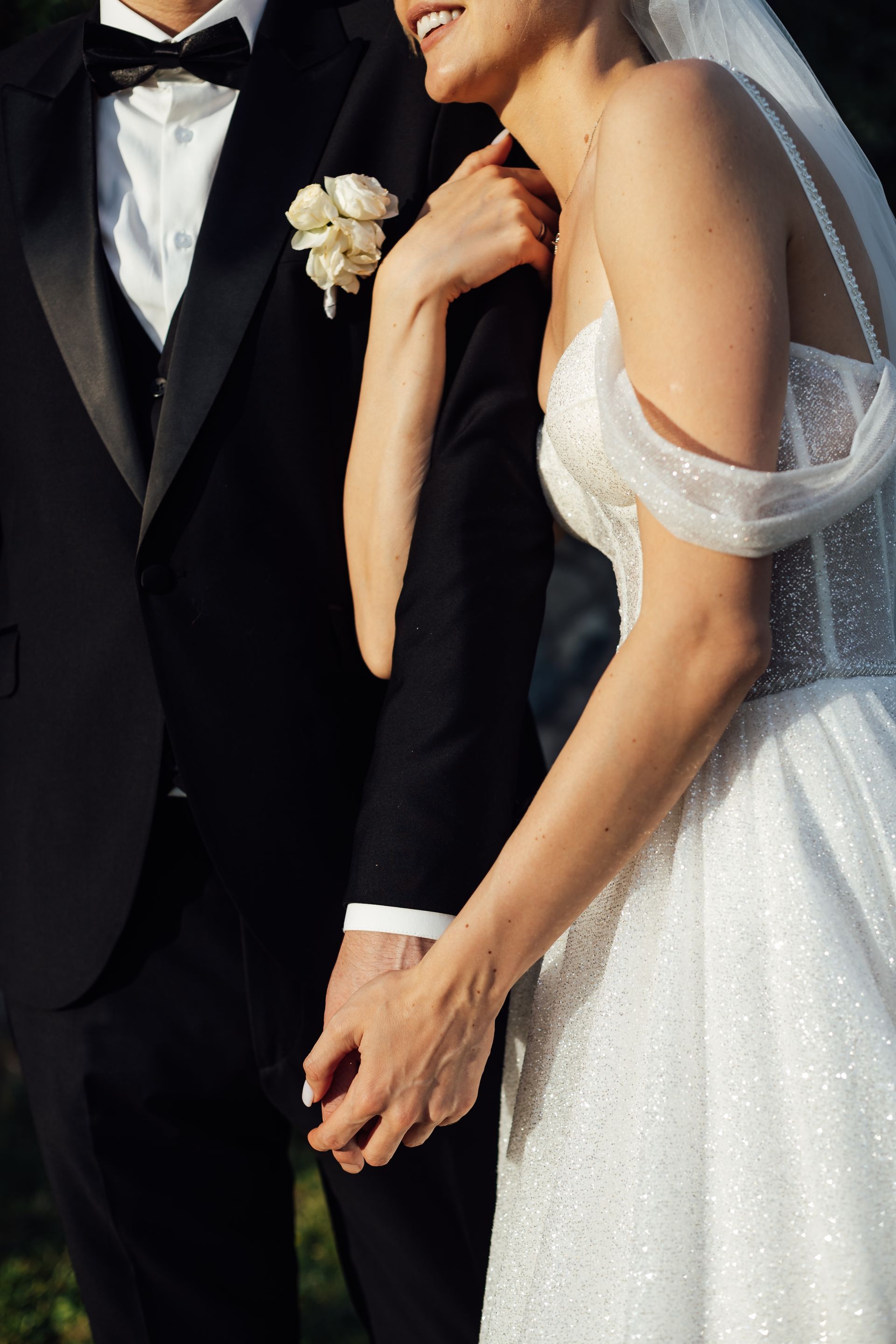 Bride and groom in formal attire embrace. Groom in black tuxedo, bride in white wedding dress, holding hands.