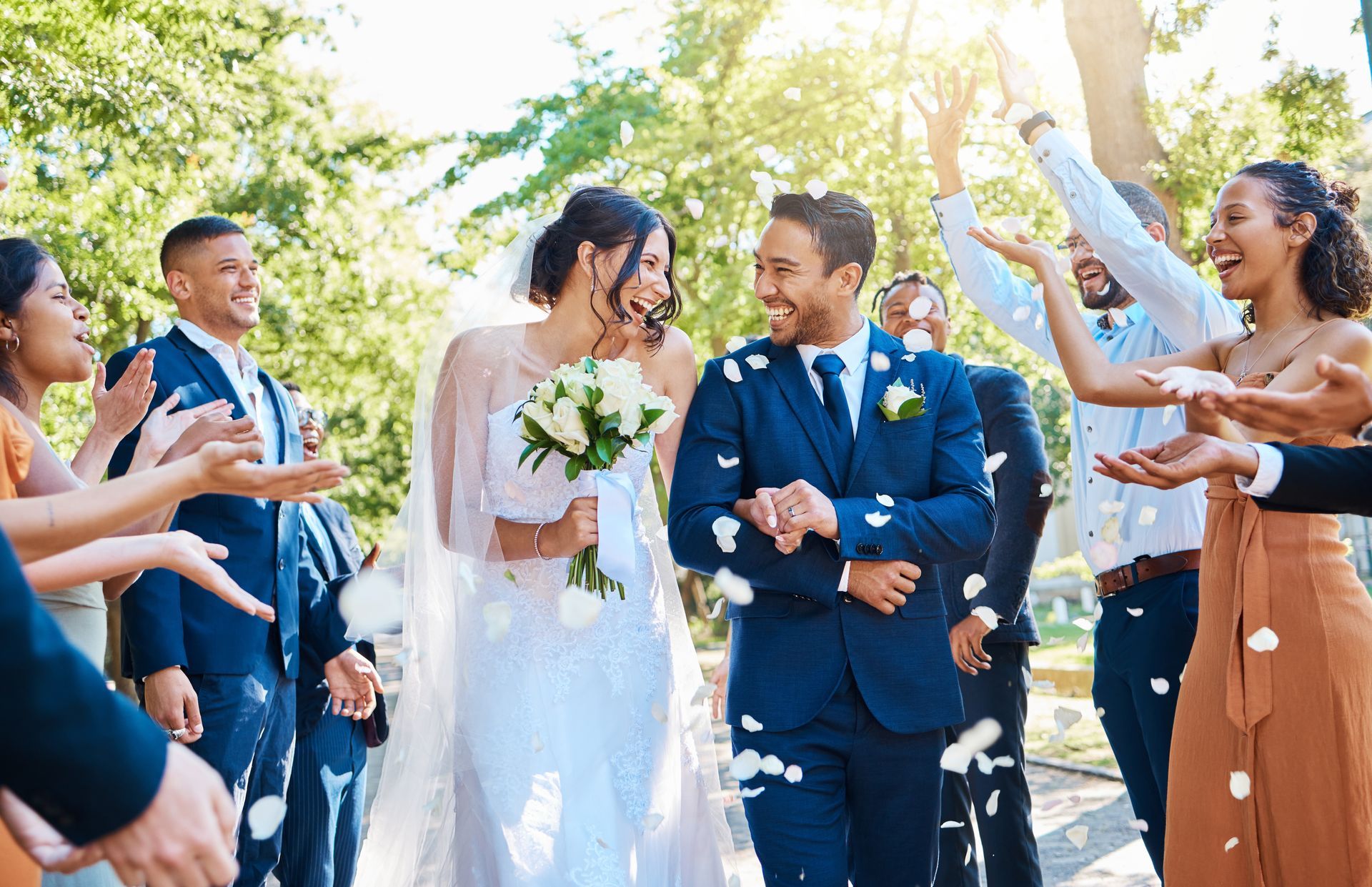 Newlyweds walk through guests throwing confetti; sunny outdoor setting.
