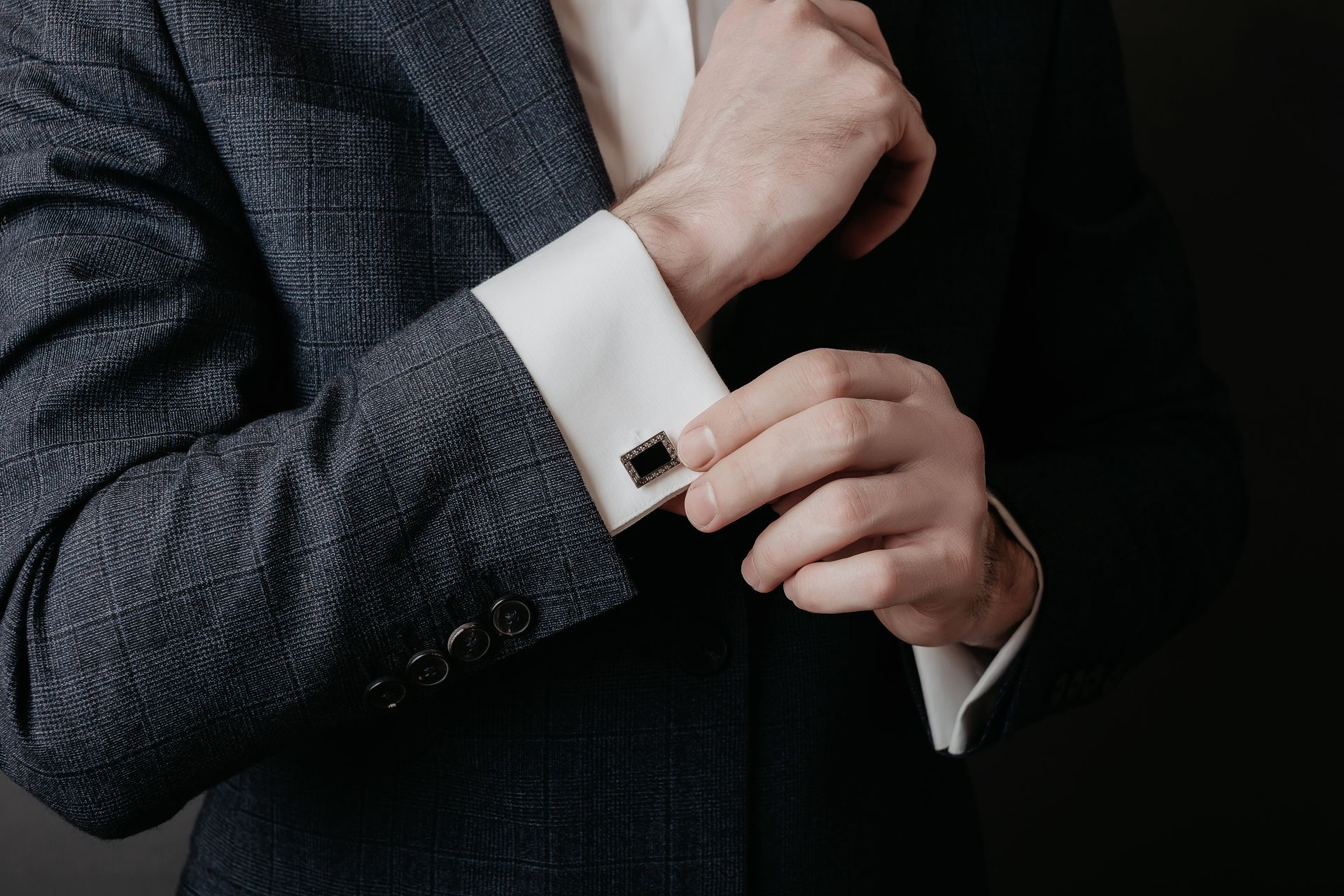 Man in suit adjusting cufflinks, with white shirt cuffs and black cufflinks visible.