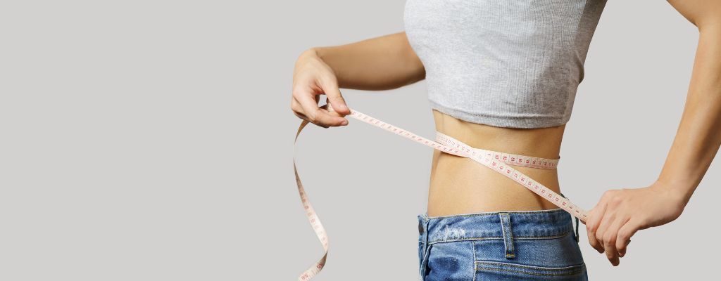 A woman is measuring her waist with a tape measure.