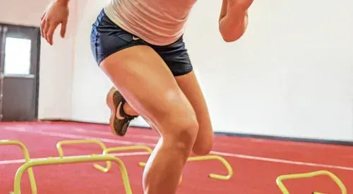 A person running over yellow hurdles on an indoor track.