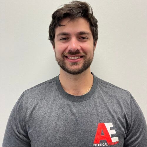 A man with a beard is wearing a gray ae physical therapy shirt.