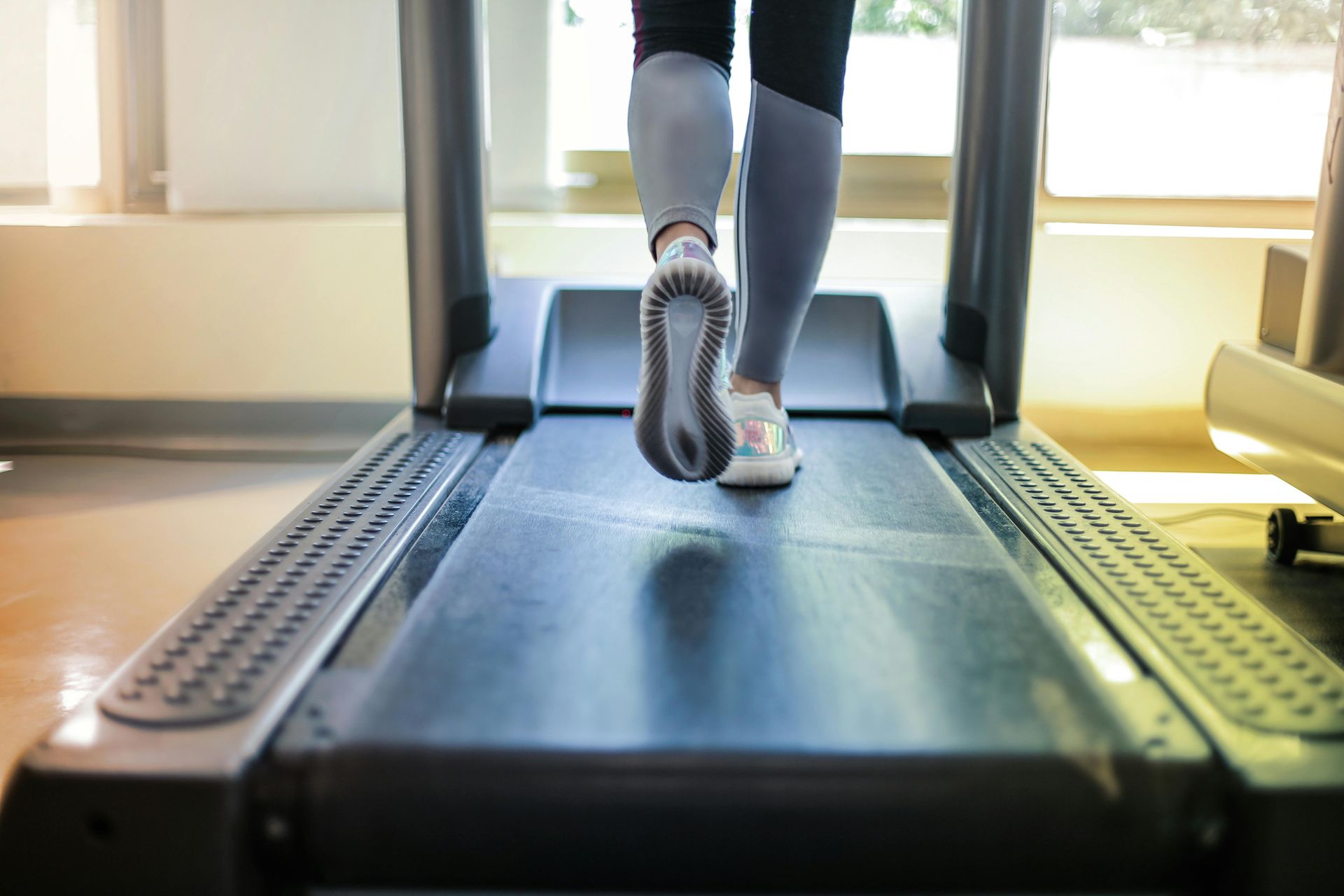 Person running on a treadmill in a brightly lit gym. Focus on feet and the moving treadmill belt.