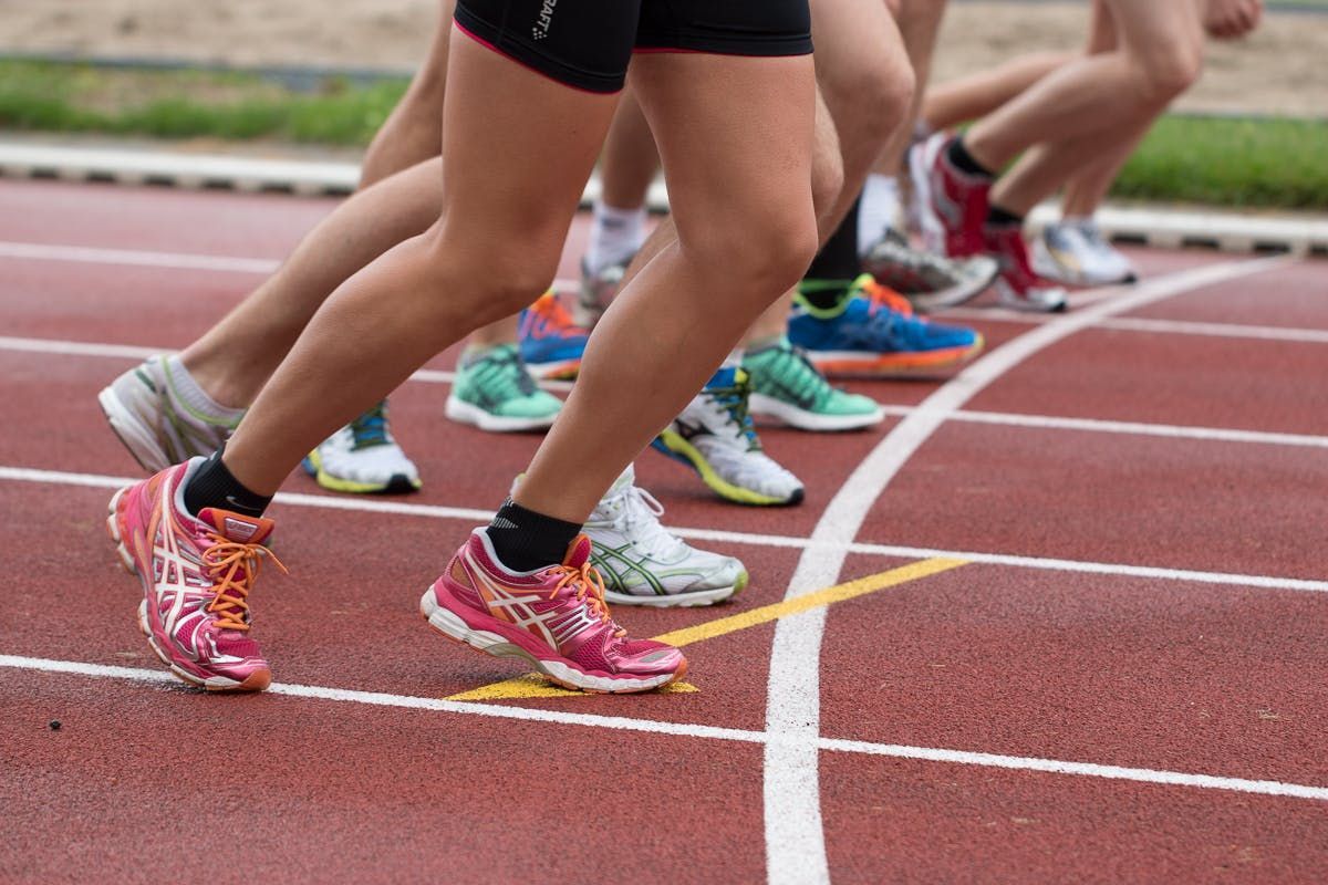 Runners in colorful sneakers on a red track, legs in motion, starting a race.
