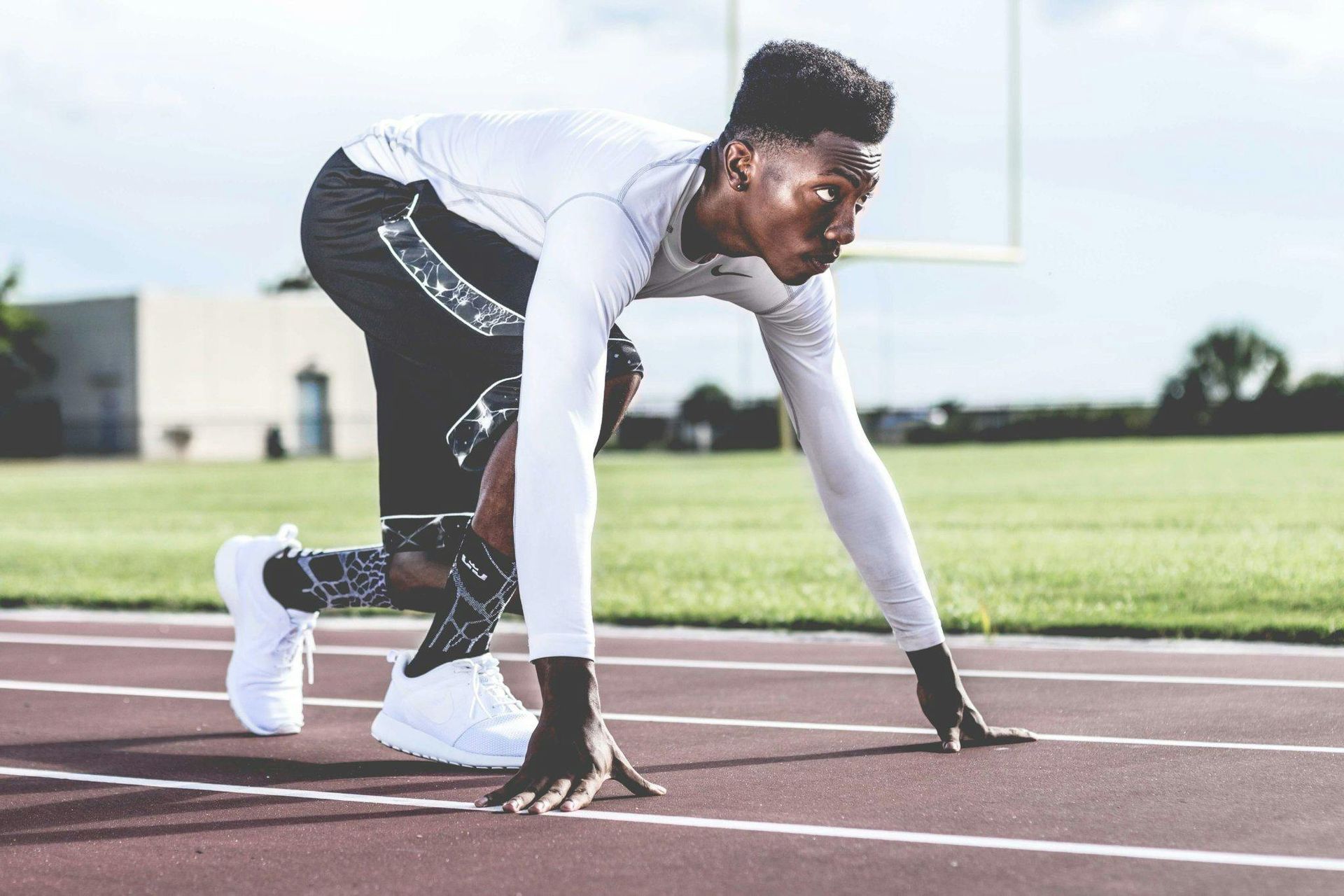 Runner in starting position on a track, wearing white athletic gear, with focused expression.