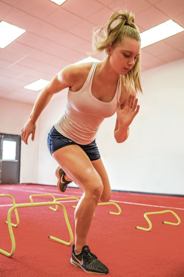A woman is jumping over hurdles in a gym.