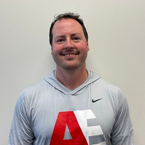 A man wearing a grey nike shirt with the letter a on it is smiling for the camera.