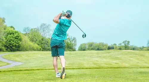 A man is swinging a golf club on a golf course.