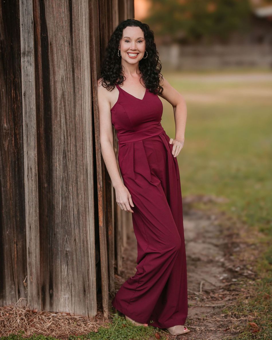 A woman in a maroon jumpsuit is leaning against a wooden fence.
