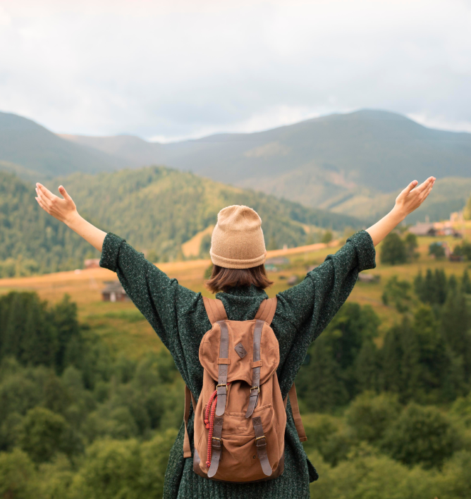 A woman with a backpack is standing on top of a hill with her arms outstretched.