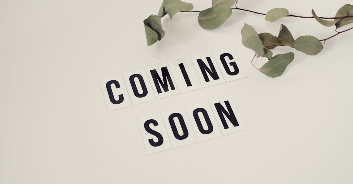 A sign that says `` coming soon '' next to a branch of eucalyptus leaves.