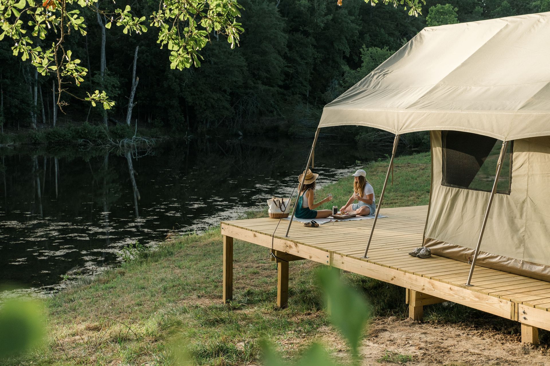Two people are sitting on a wooden deck next to a tent.