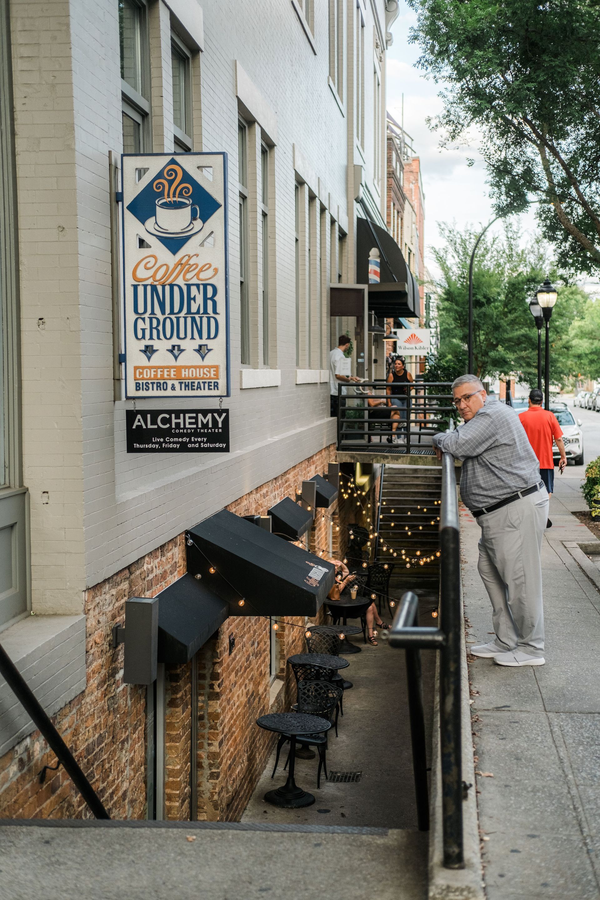 A man standing on a sidewalk in front of a building with a sign that says coffee underground