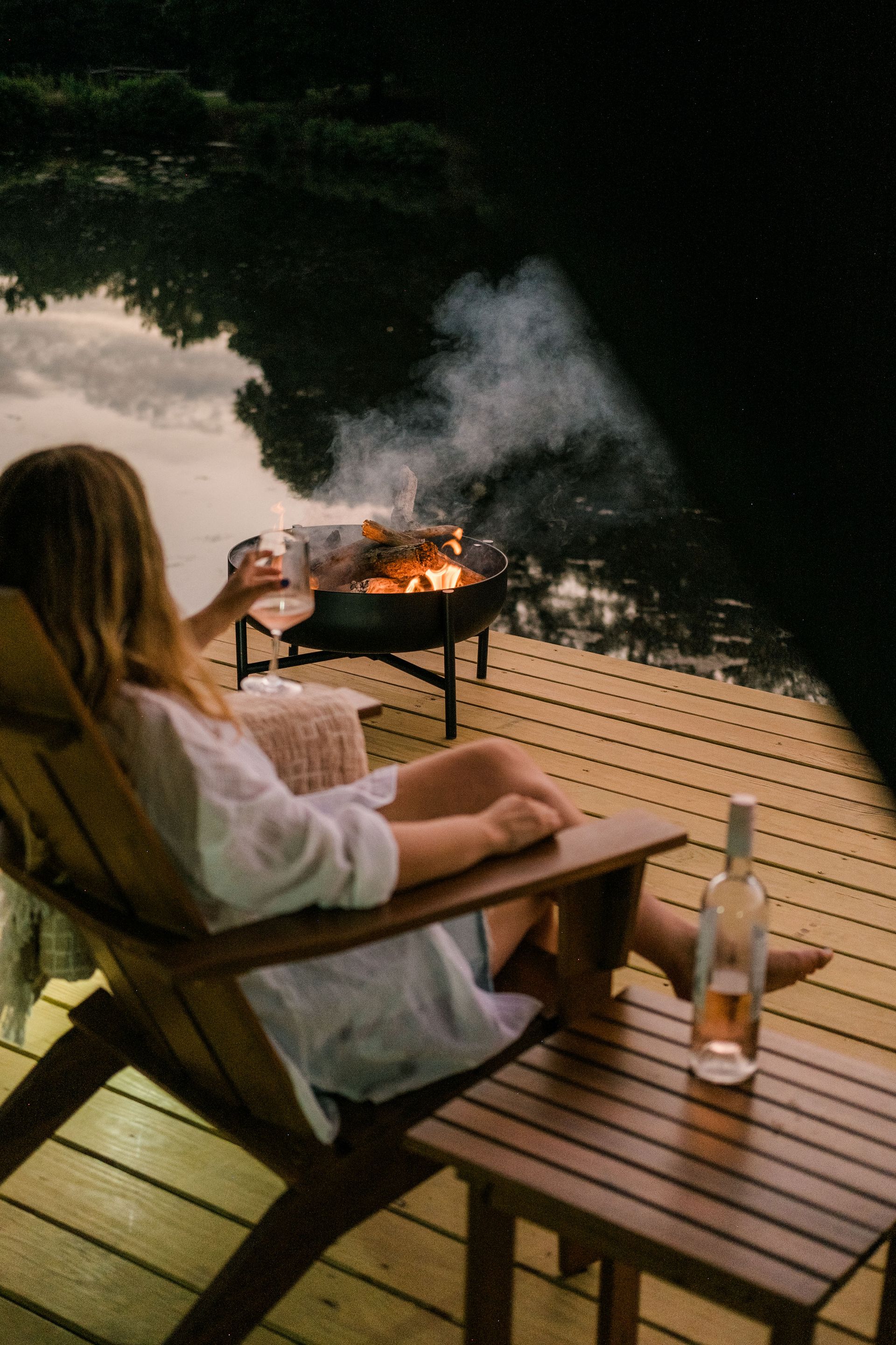 A woman is sitting in a chair on a dock holding a glass of wine.