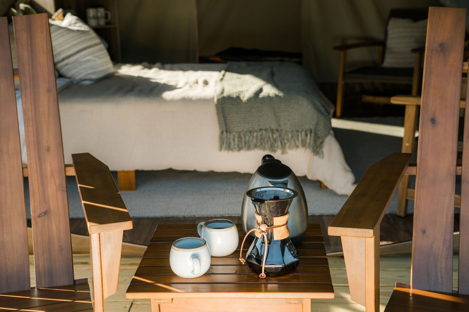 Two wooden chairs are sitting next to a wooden table in front of a bed.