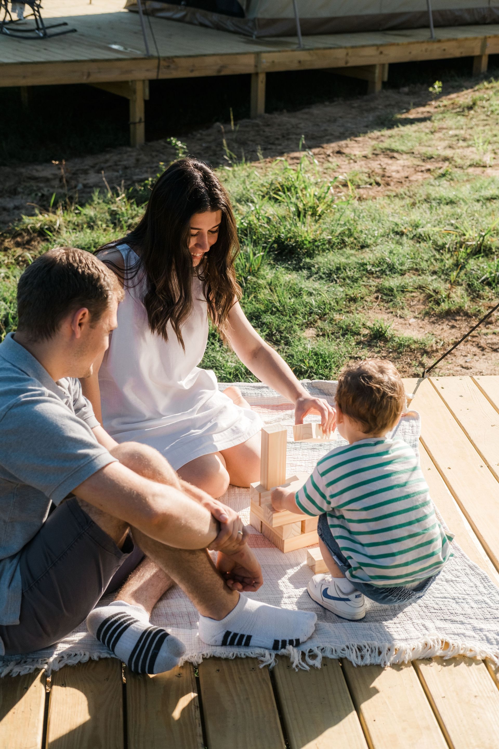 A family is sitting on a blanket on a deck playing with blocks.