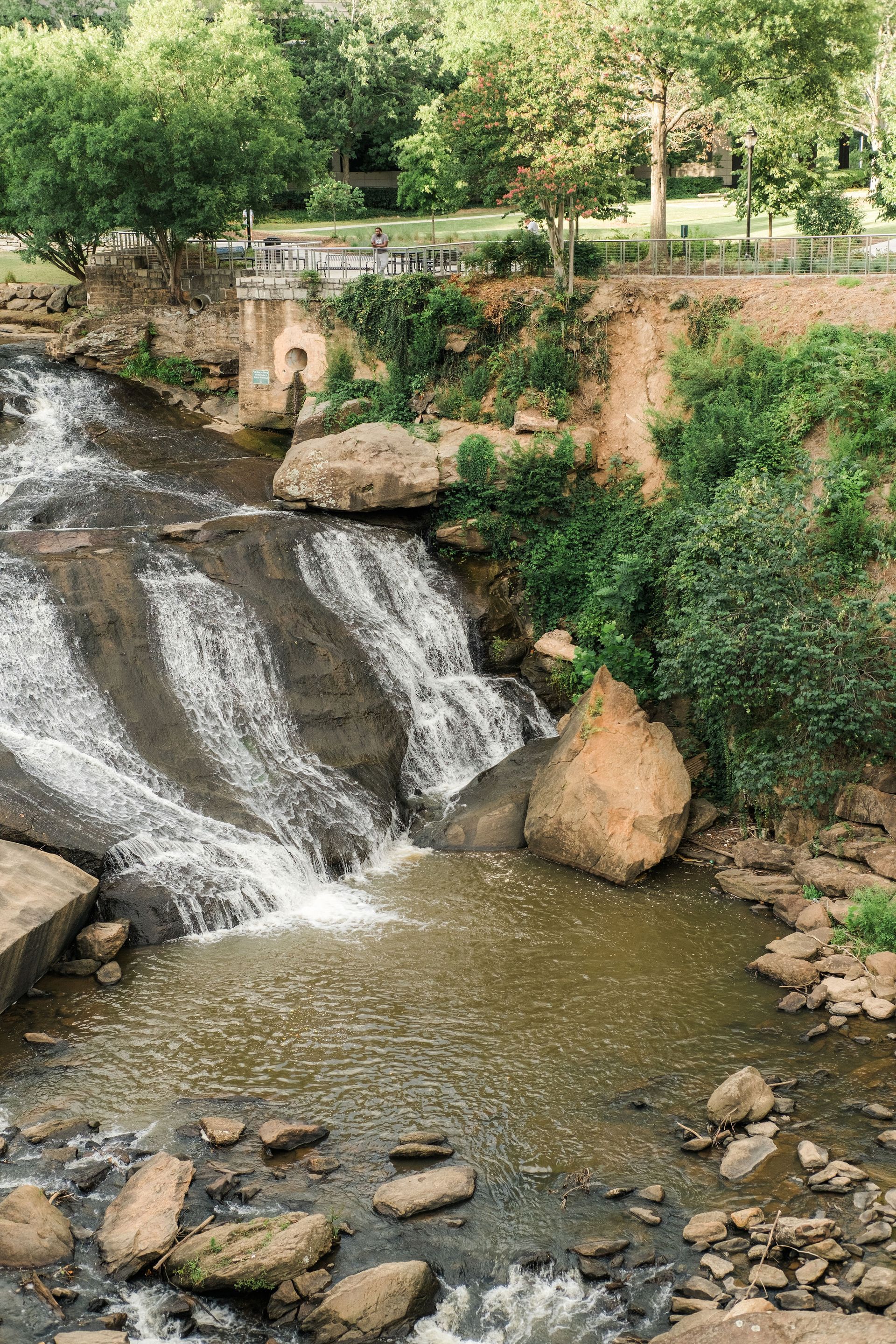 A waterfall is surrounded by rocks and trees in a park.