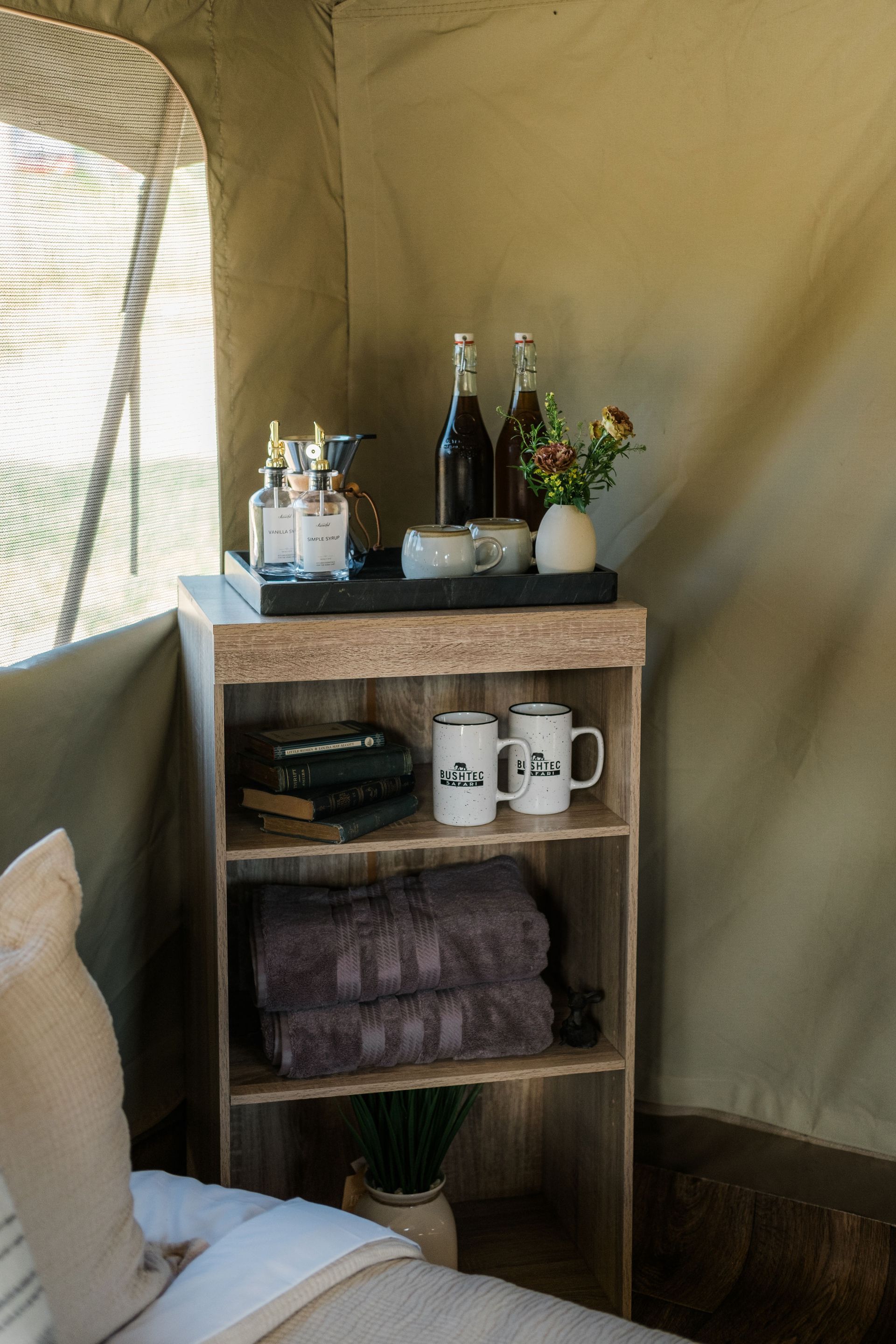 A wooden shelf with bottles and mugs on it in a tent.