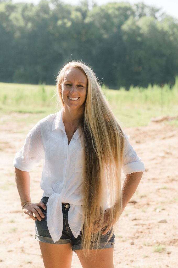 A woman with very long hair is standing in a field with her hands on her hips.