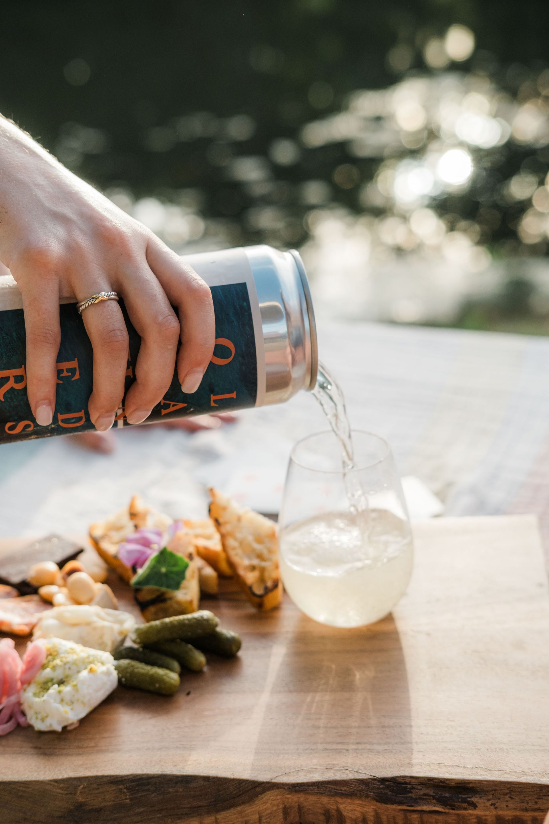 A person is pouring a drink into a glass on a cutting board.