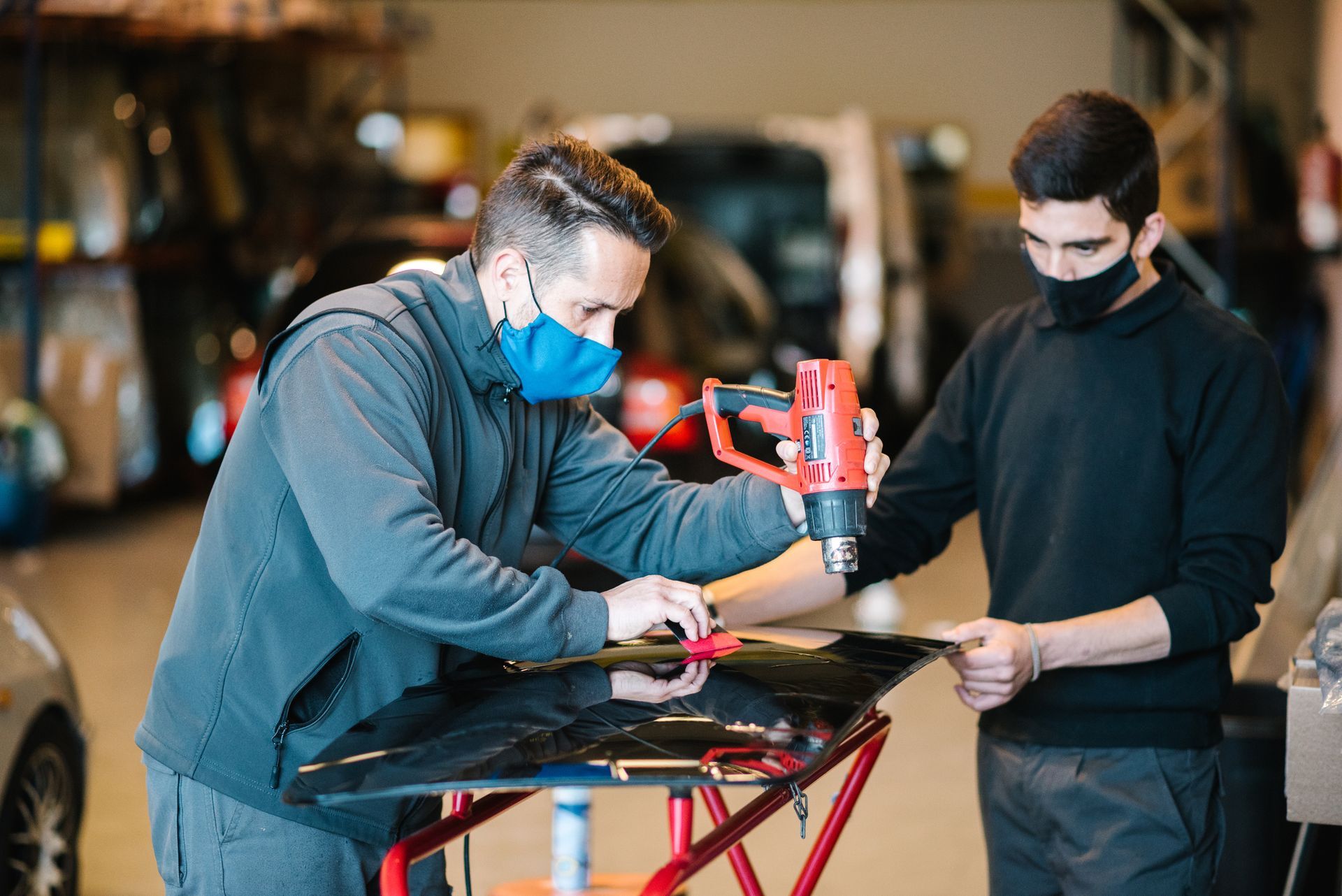 Two men wearing masks are working on a car in a garage - Drummond, MT - Big Sky Auto Glass and Screens