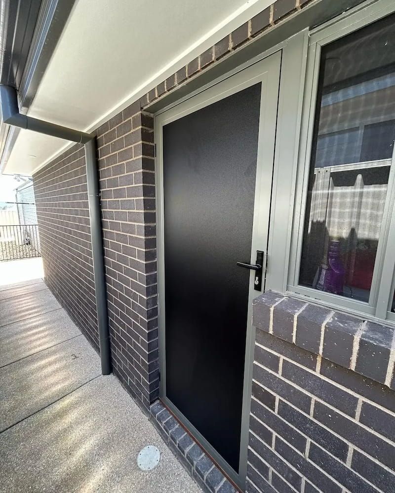 Grey Security Door With Black Mesh, Mounted in a Brick Wall — Ingrams Installations in Wagga Wagga, NSW