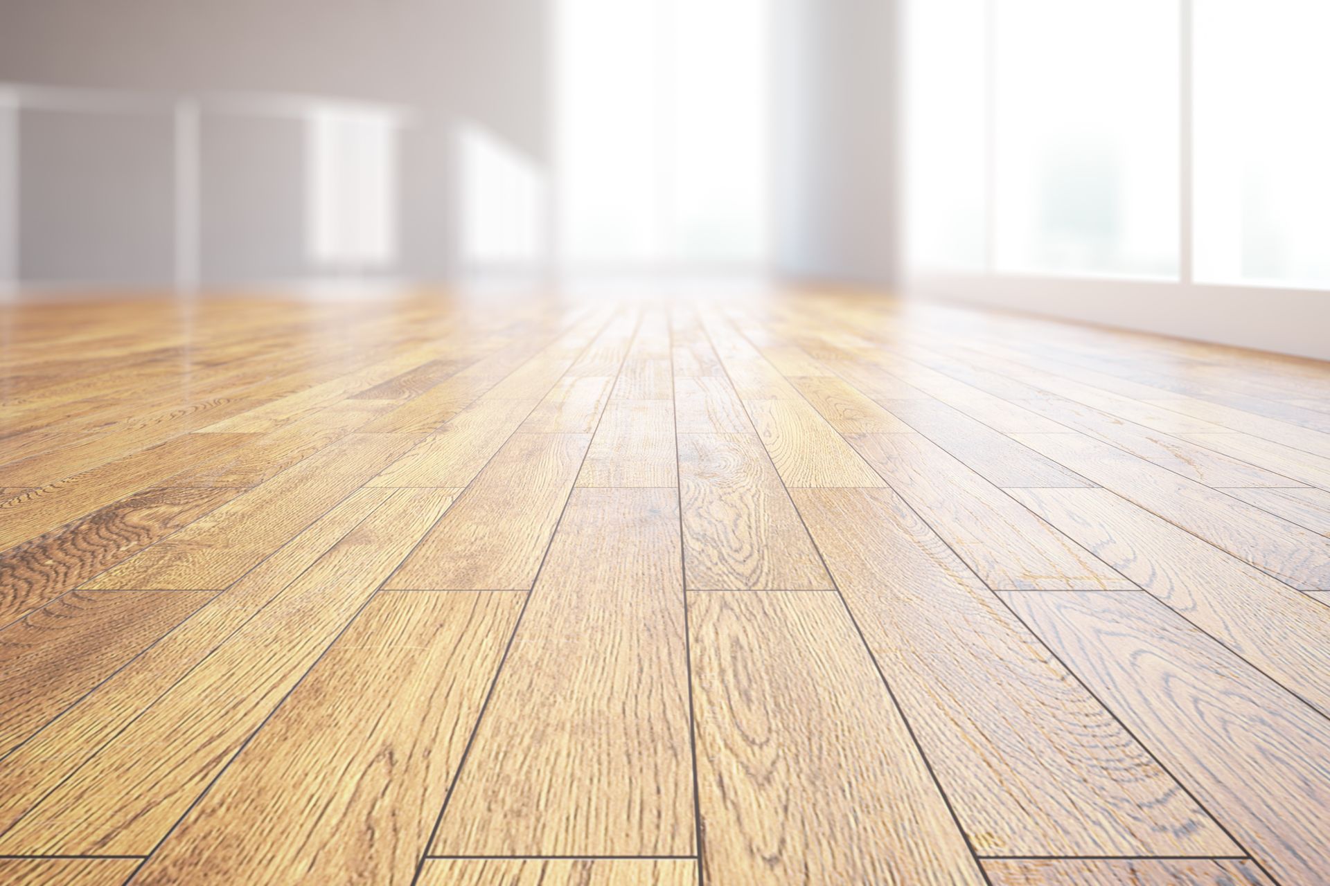 Wooden floor in a bright, empty room with blurred windows and sunlight.