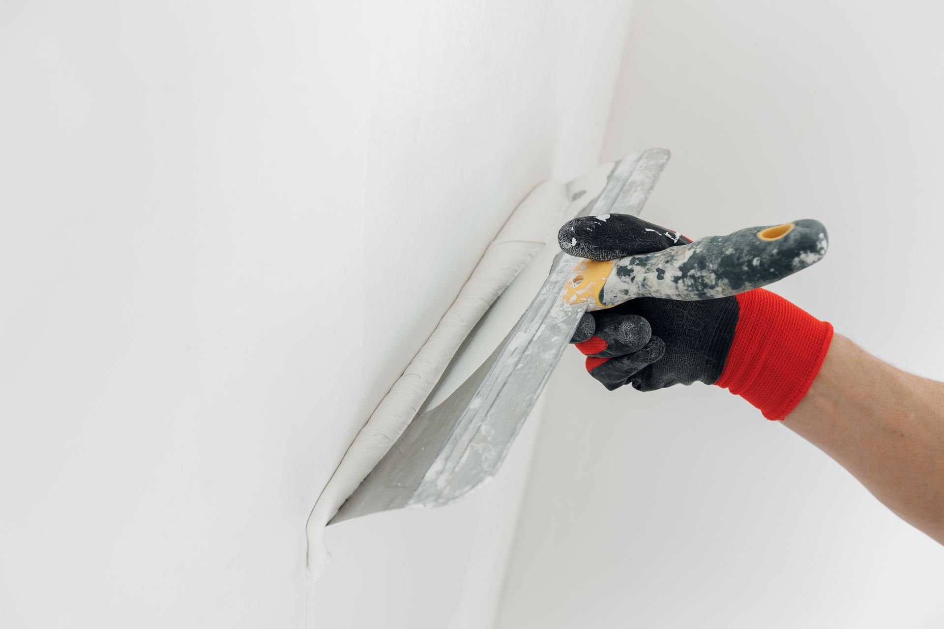 Person smoothing white plaster on a wall with a metal trowel.