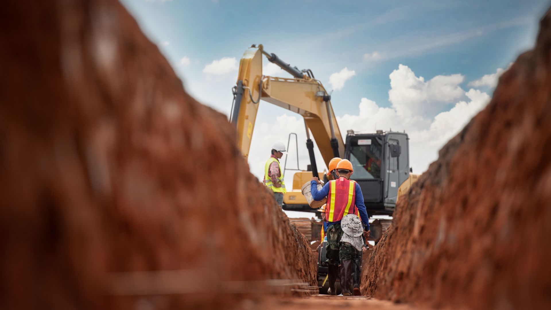 A group of construction workers are digging a trench with a bulldozer in the background.