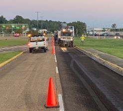 A group of trucks are driving down a road next to orange cones.