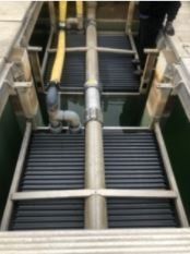 A man is standing in a drain with a bunch of pipes coming out of it.