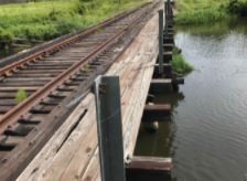 A wooden bridge over a river next to train tracks.