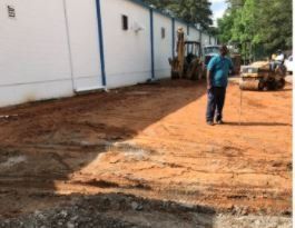 A man is standing on a dirt road in front of a building.