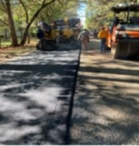 A road is being paved in a park with trees in the background.