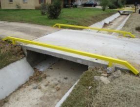 A concrete bridge with yellow railings over a drain.