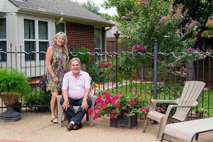 A man and a woman are sitting on a patio in front of a house.