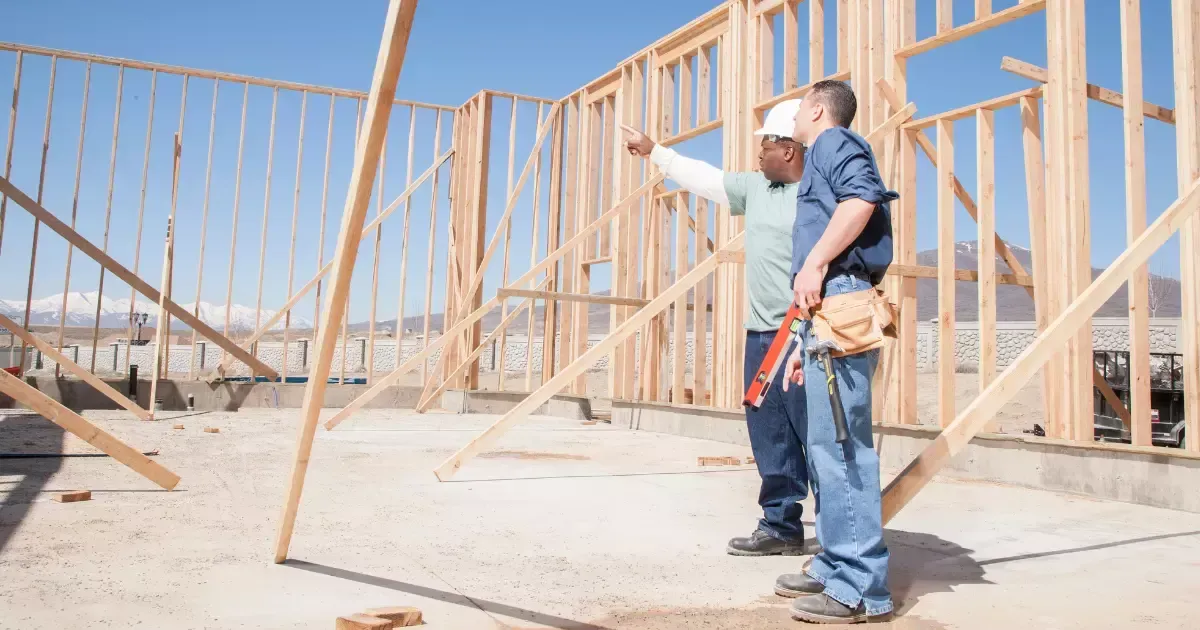 Builders reviewing a home addition plan at a framed construction site