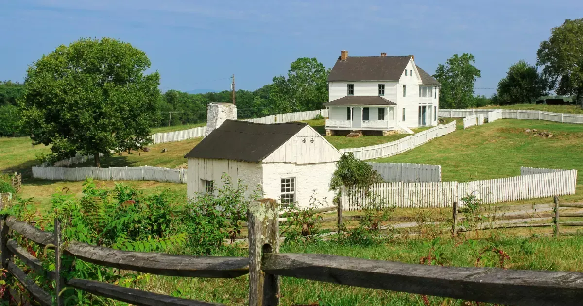 Classic white farmhouse with wide porch and fencing, reflecting timeless modern farmhouse home designs