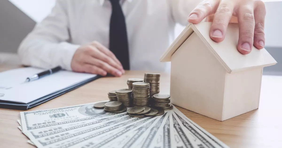 Hand holding house beside stacked coins and cash