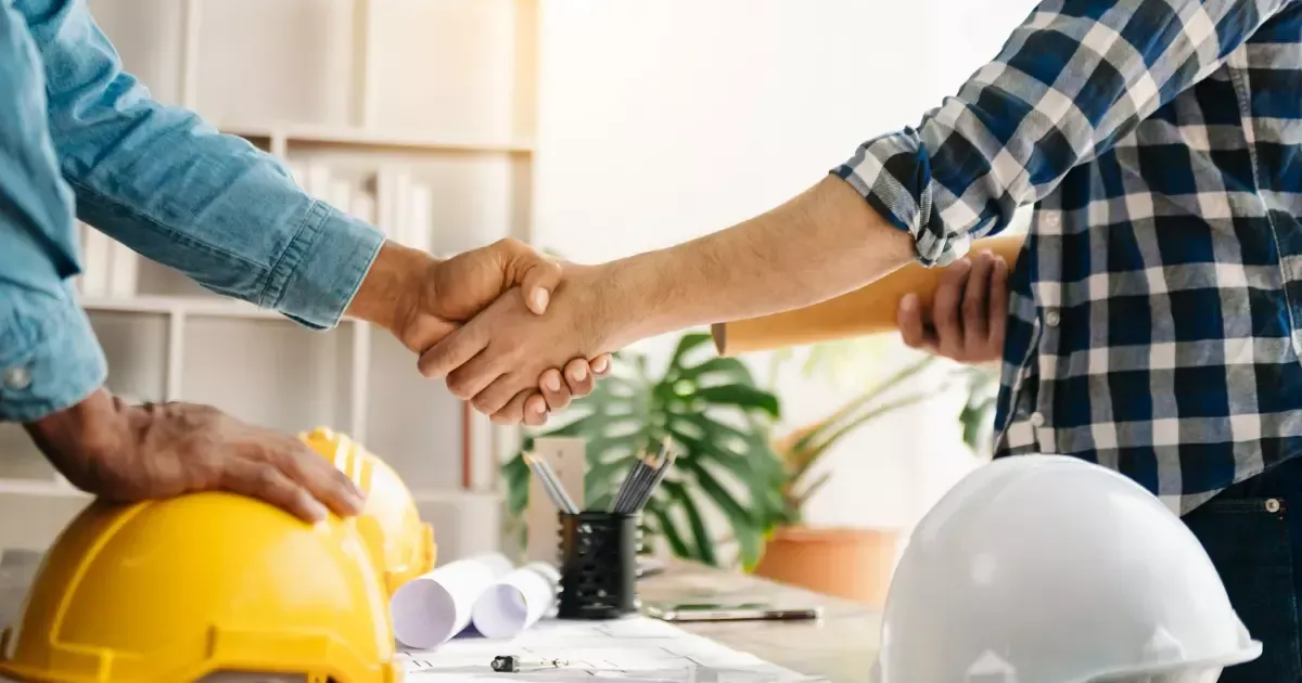 Handshake over blueprints and hard hat